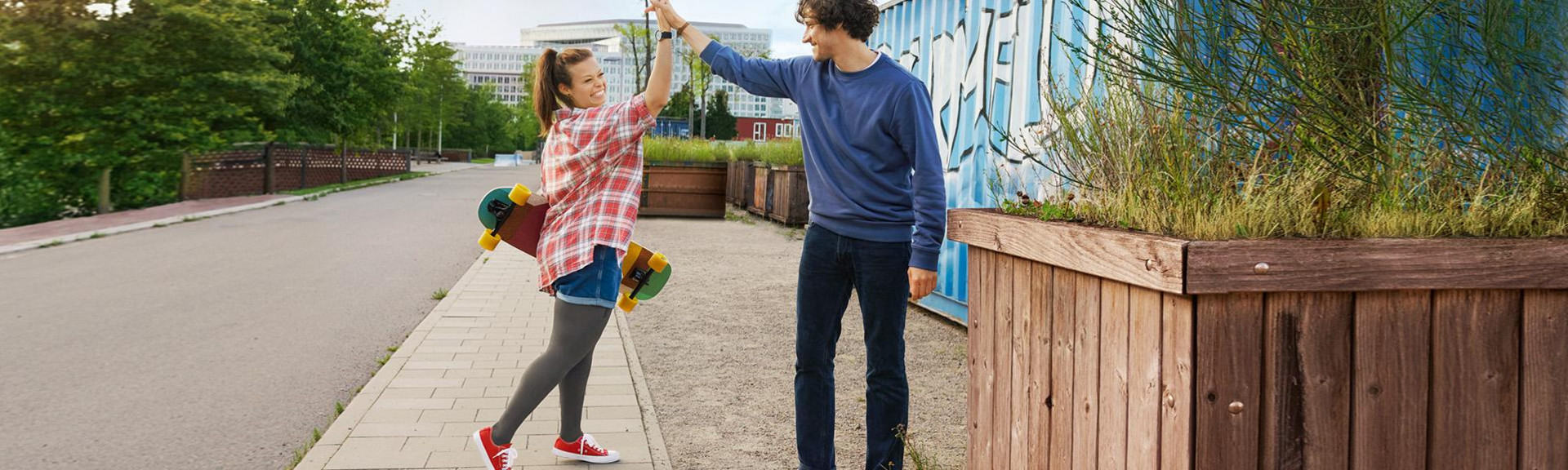 Young woman holding skateboard and young male high five each other as walking in a street