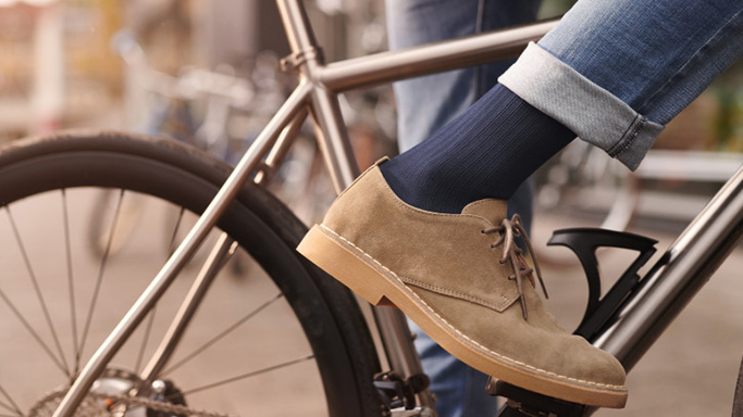 Close up of men's foot in beige shoe with blue compression socks and jeans on the peddle of a bicycle